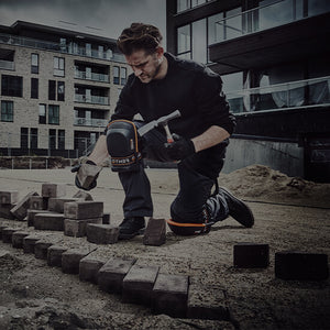 Man wearing a pair of Fento knee pads, holding a hammer in one hand and a block of stone in the other